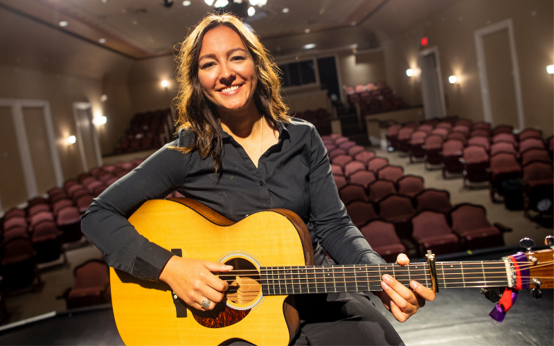 Woman with guitar sitting on theatre stage